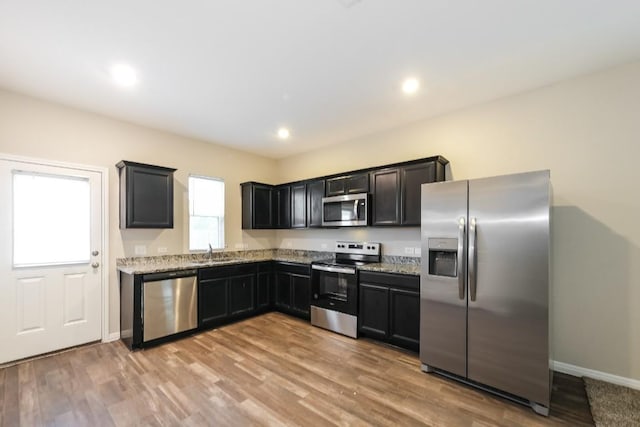 kitchen with light stone countertops, appliances with stainless steel finishes, sink, and light hardwood / wood-style floors