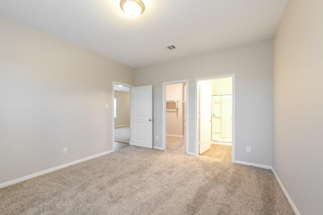 unfurnished bedroom featuring connected bathroom, a spacious closet, light colored carpet, and a closet