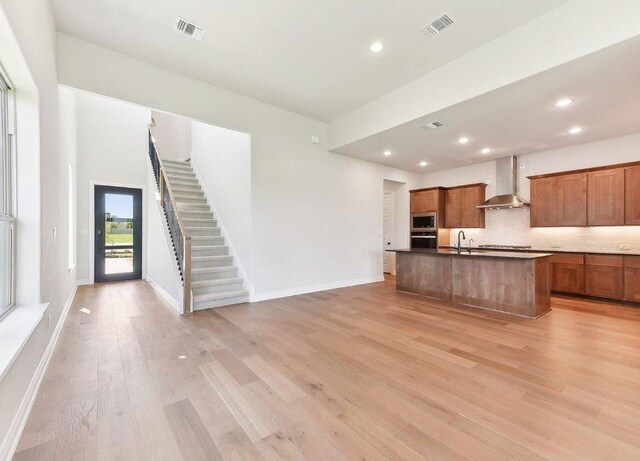 232 Flora Springs Cv, Liberty Hill, TX 78642 - kitchen featuring wall chimney range hood, light wood finished floors, visible vents, and stainless steel microwave