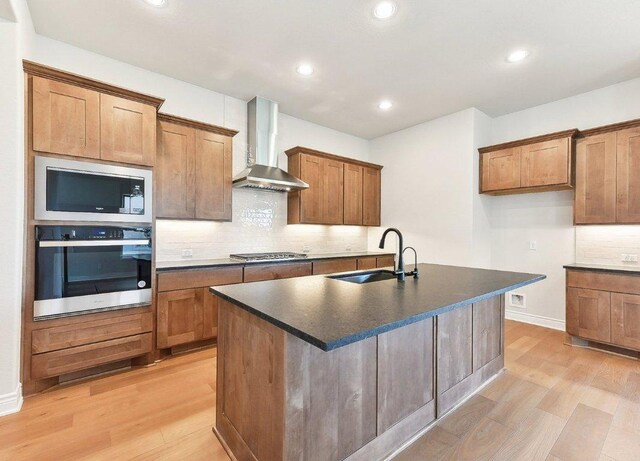 232 Flora Springs Cv, Liberty Hill, TX 78642 - kitchen featuring light wood-style flooring, wall chimney range hood, appliances with stainless steel finishes, a sink, and dark countertops