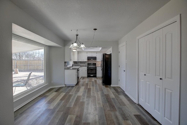 kitchen featuring black fridge, hanging light fixtures, backsplash, stove, and white cabinets