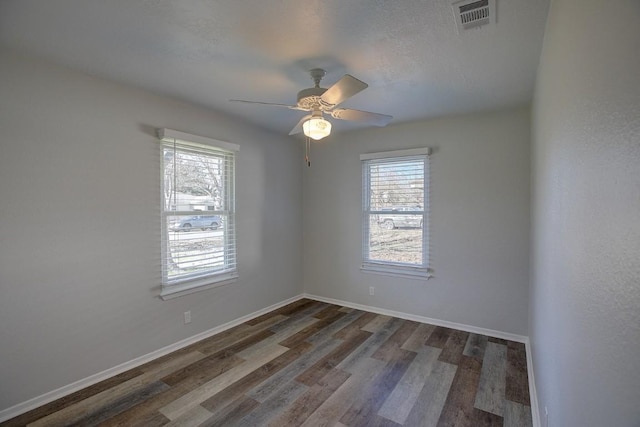 spare room featuring dark wood-type flooring, a wealth of natural light, and ceiling fan