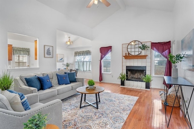 living room featuring high vaulted ceiling, beamed ceiling, a tiled fireplace, hardwood / wood-style flooring, and ceiling fan