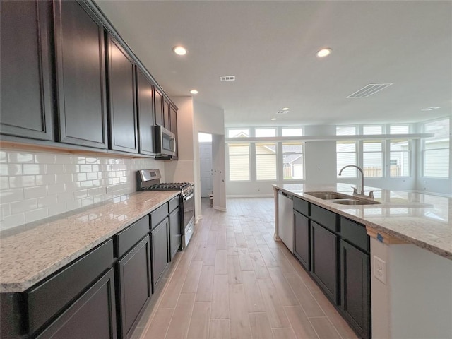 kitchen featuring sink, light hardwood / wood-style flooring, stainless steel appliances, light stone countertops, and decorative backsplash