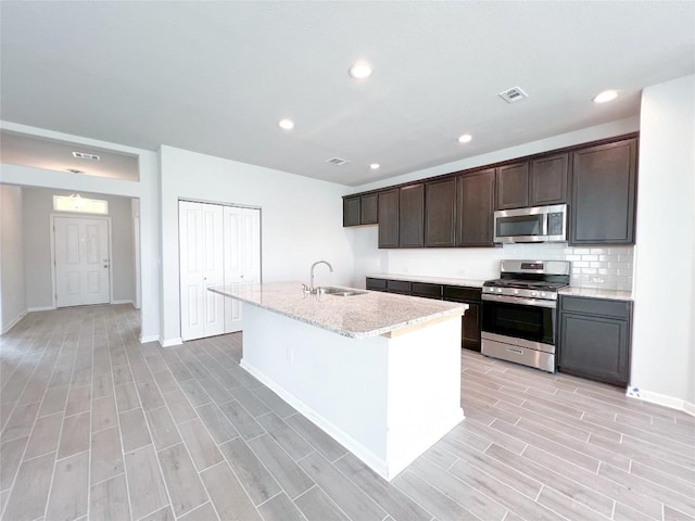 kitchen with sink, dark brown cabinets, stainless steel appliances, and an island with sink