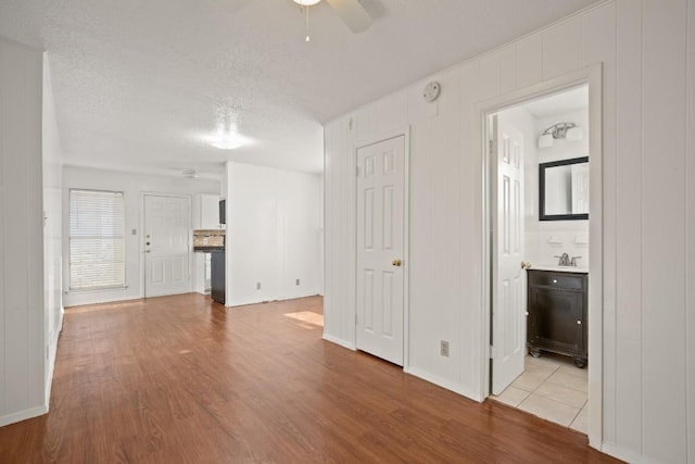 unfurnished living room with sink, a textured ceiling, light hardwood / wood-style floors, and ceiling fan