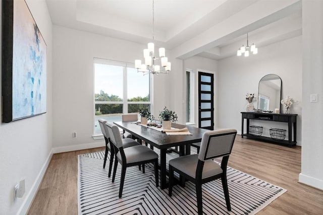 dining room with a chandelier, light wood-type flooring, a raised ceiling, and baseboards