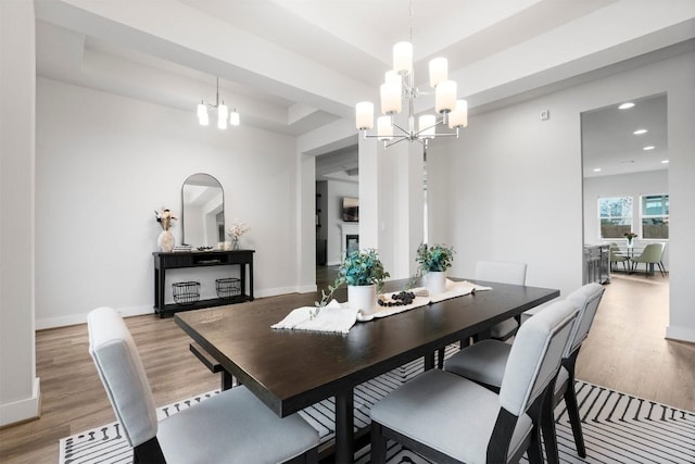 dining area with a fireplace, baseboards, light wood-style floors, a tray ceiling, and an inviting chandelier