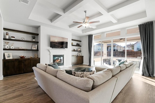 living room with coffered ceiling, ceiling fan, dark wood finished floors, and a glass covered fireplace