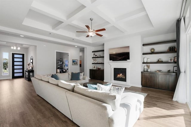 living room with a warm lit fireplace, coffered ceiling, beamed ceiling, and wood finished floors