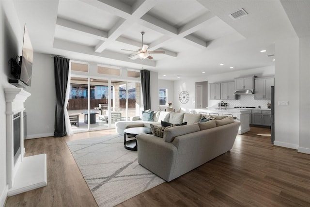 living room featuring a glass covered fireplace, dark wood-style flooring, visible vents, and baseboards