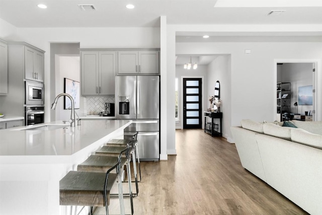 kitchen featuring stainless steel appliances, visible vents, a kitchen breakfast bar, light countertops, and gray cabinets