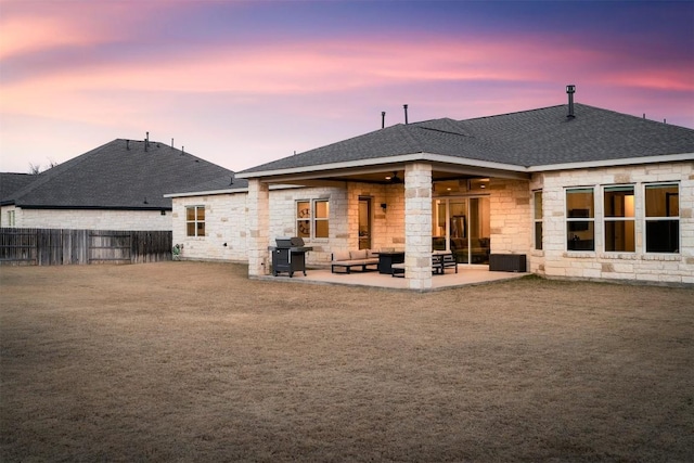 rear view of house with a patio, a shingled roof, stone siding, and fence