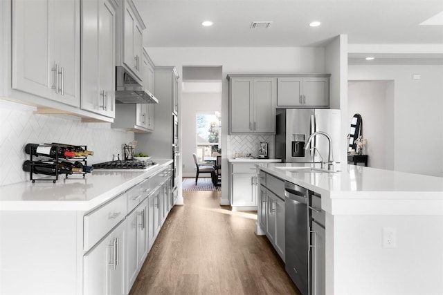 kitchen with a kitchen island with sink, under cabinet range hood, stainless steel appliances, visible vents, and light countertops