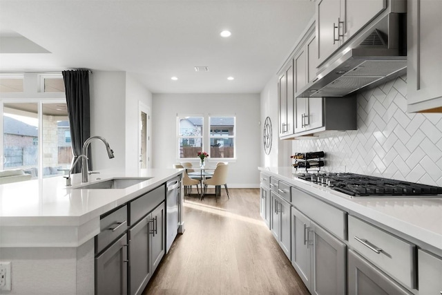 kitchen with stainless steel appliances, gray cabinets, light countertops, a sink, and under cabinet range hood