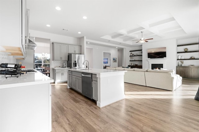 kitchen with stainless steel appliances, light countertops, gray cabinetry, open floor plan, and a kitchen island with sink