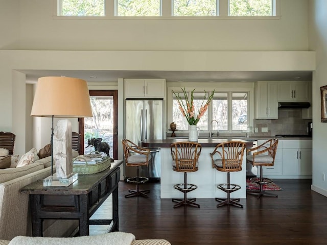 kitchen with dark wood-type flooring, white cabinetry, stainless steel fridge, a towering ceiling, and decorative backsplash