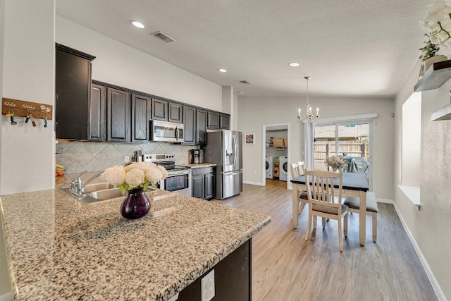 kitchen with stainless steel appliances, lofted ceiling, light stone counters, and independent washer and dryer