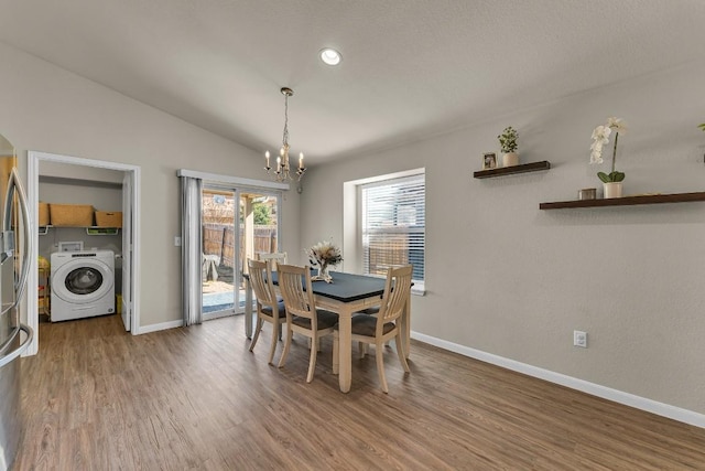 dining space with hardwood / wood-style flooring, lofted ceiling, washer / clothes dryer, and an inviting chandelier