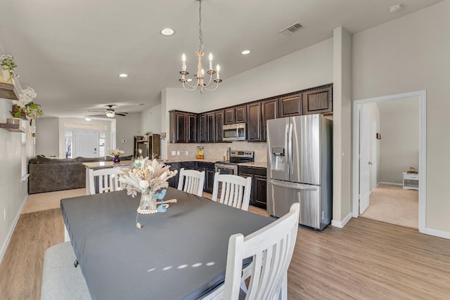 dining area with ceiling fan with notable chandelier and light hardwood / wood-style flooring