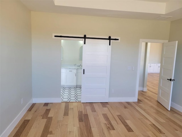 unfurnished bedroom with a barn door, sink, and light hardwood / wood-style flooring