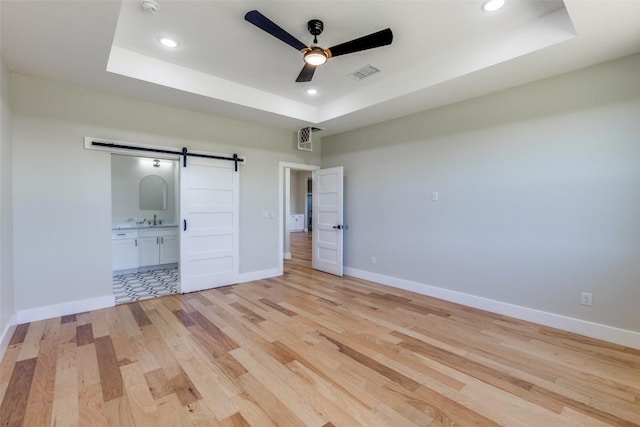 unfurnished bedroom featuring a barn door, a raised ceiling, light wood-style floors, recessed lighting, and visible vents