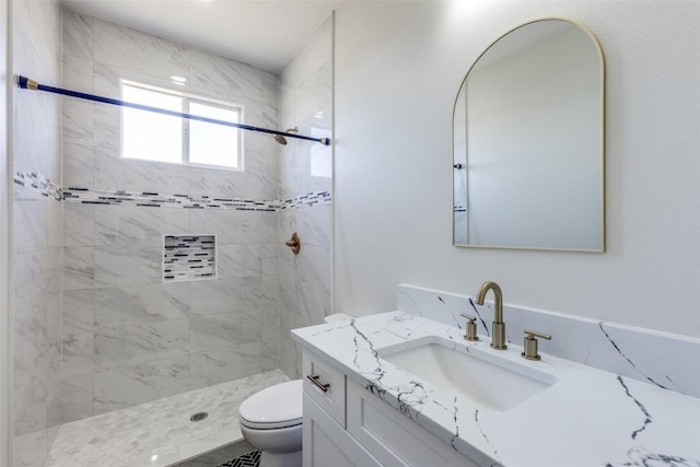 bathroom with toilet, tiled shower, and vanity