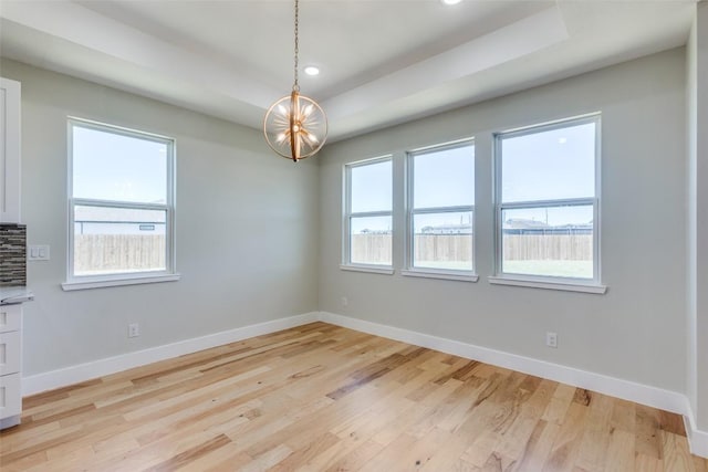 spare room featuring baseboards, a tray ceiling, light wood-style flooring, and a notable chandelier