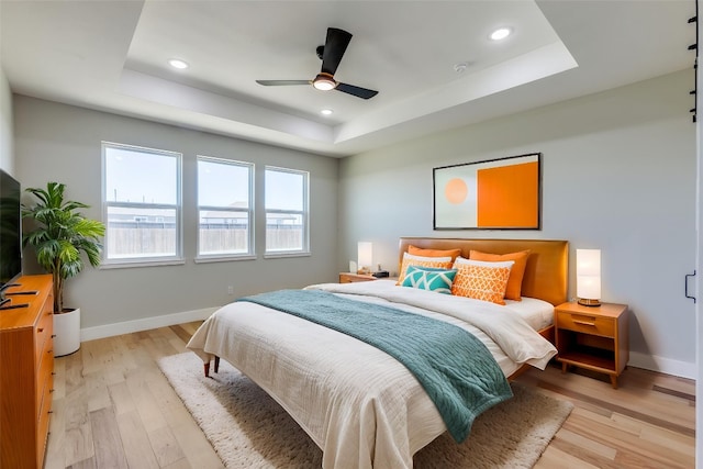 bedroom with baseboards, a tray ceiling, recessed lighting, and light wood-style flooring
