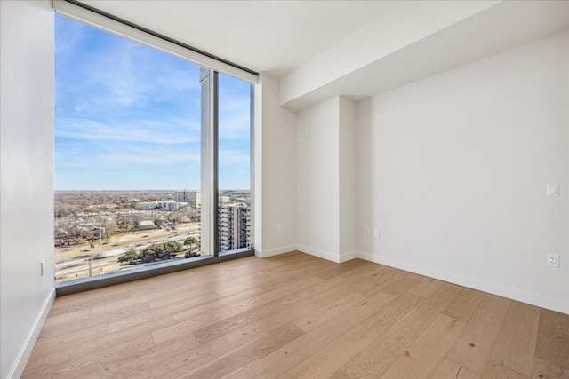 spare room with a wall of windows and light hardwood / wood-style floors