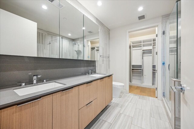 44 E Ave Unit 1407, Austin, TX 78701 - full bathroom with a walk in closet, toilet, a shower stall, double vanity, and decorative backsplash