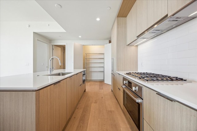 kitchen with sink, light hardwood / wood-style flooring, a center island with sink, light brown cabinets, and appliances with stainless steel finishes