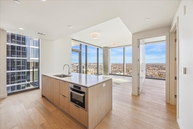 kitchen with sink, oven, a kitchen island with sink, light hardwood / wood-style floors, and light brown cabinets