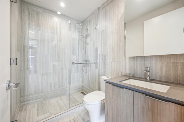 bathroom with a shower with door, tile walls, vanity, tasteful backsplash, and toilet