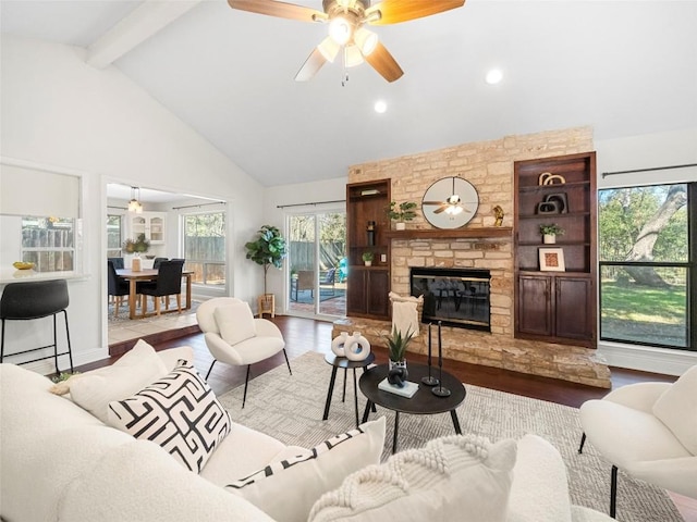 living room featuring hardwood / wood-style flooring, ceiling fan, high vaulted ceiling, a stone fireplace, and beamed ceiling