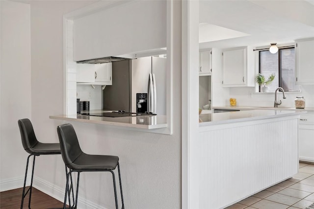 kitchen with white cabinets, stainless steel fridge with ice dispenser, a breakfast bar, light countertops, and a sink