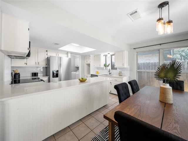 kitchen featuring light tile patterned floors, a peninsula, separate washer and dryer, a sink, and stainless steel refrigerator with ice dispenser