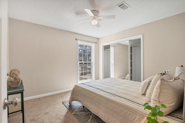 carpeted bedroom with a closet, visible vents, a ceiling fan, a textured ceiling, and baseboards