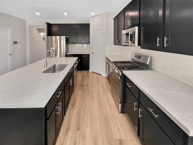 kitchen featuring an island with sink, appliances with stainless steel finishes, sink, and light hardwood / wood-style flooring