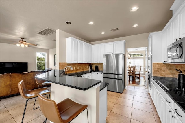 kitchen with appliances with stainless steel finishes, white cabinetry, a kitchen breakfast bar, light tile patterned floors, and kitchen peninsula