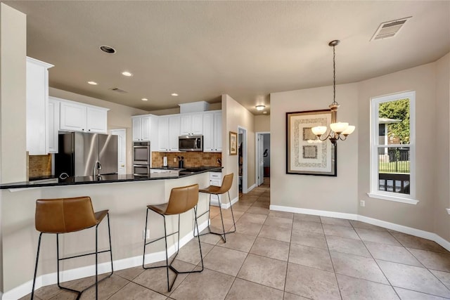 kitchen with appliances with stainless steel finishes, decorative light fixtures, white cabinetry, backsplash, and kitchen peninsula