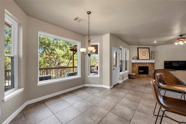 dining area with ceiling fan with notable chandelier, a fireplace, and light tile patterned flooring