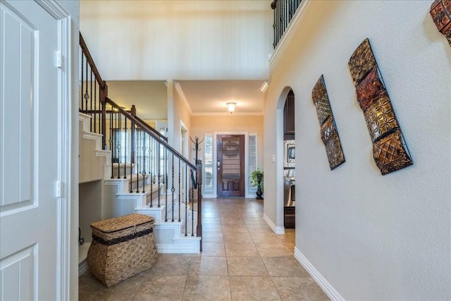 foyer featuring light tile patterned floors, a towering ceiling, and ornamental molding