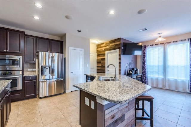 kitchen with a breakfast bar, sink, light stone counters, stainless steel appliances, and a center island with sink