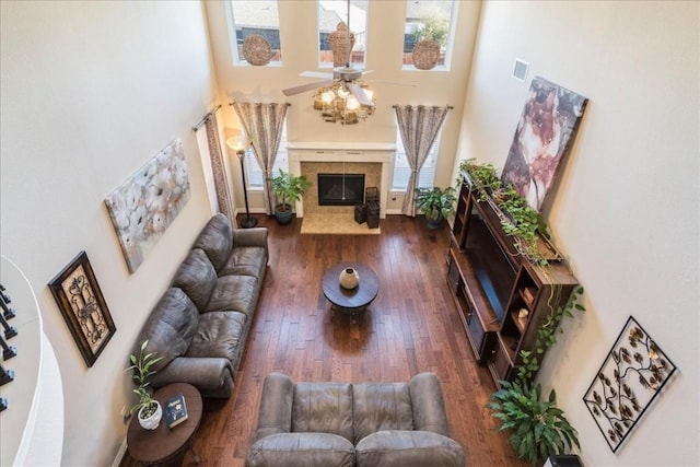 living room featuring dark wood-type flooring, a tile fireplace, ceiling fan, and a high ceiling