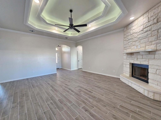 unfurnished living room featuring a fireplace, wood-type flooring, ceiling fan, a raised ceiling, and crown molding