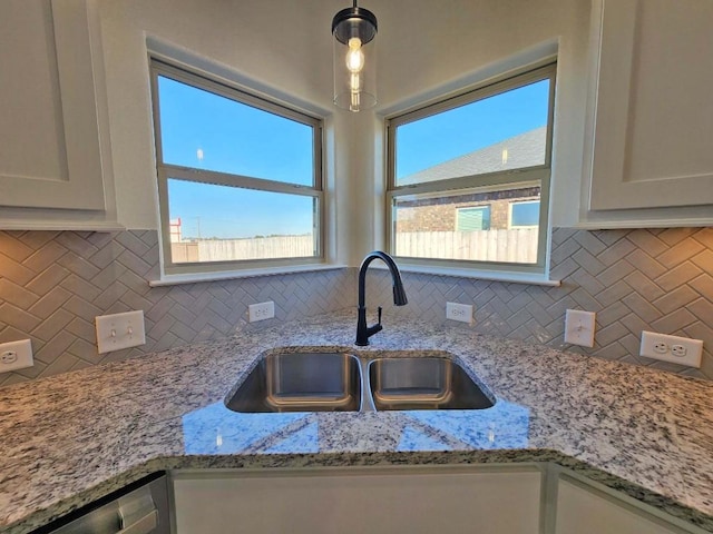 kitchen with hanging light fixtures, white cabinetry, light stone countertops, and sink