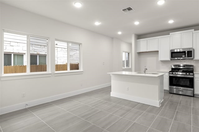 kitchen featuring appliances with stainless steel finishes, a healthy amount of sunlight, a center island with sink, and white cabinets