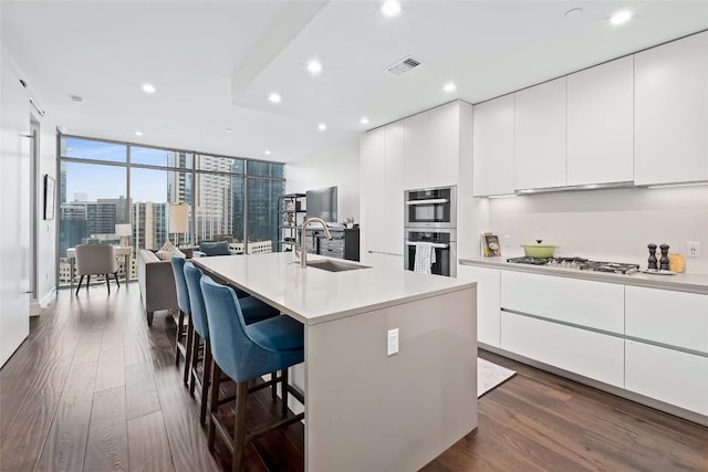 kitchen with sink, appliances with stainless steel finishes, white cabinetry, dark hardwood / wood-style floors, and an island with sink