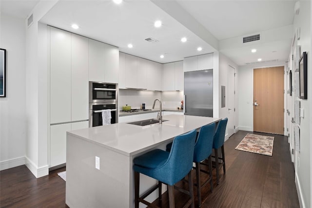 kitchen featuring sink, dark hardwood / wood-style flooring, stainless steel appliances, a kitchen island with sink, and white cabinets